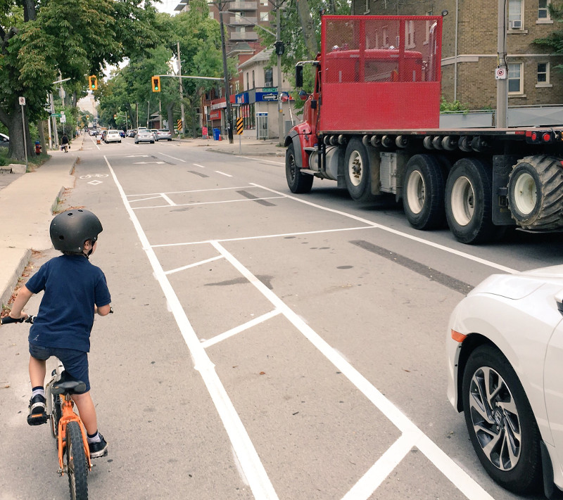 A child rides in the protected bike lanes on Herkimer while a transport truck drives past (Image Credit: Tom Flood)