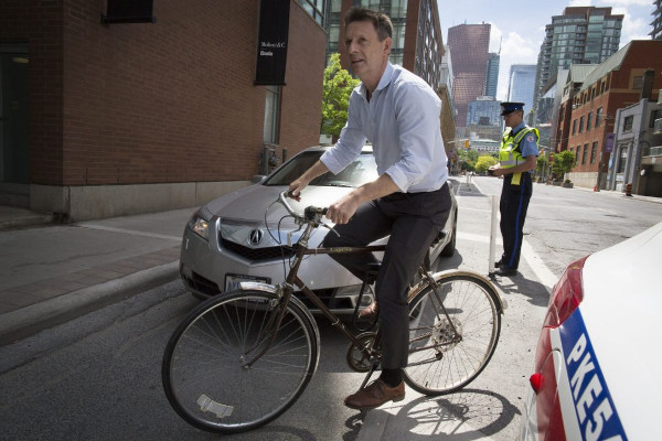 Ben Bull weaving around a car blocking the Adelaide bike lane as a police officer issues a ticket (Image Credit: Todd Korol/Toronto Star)