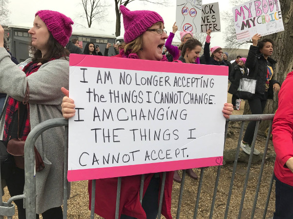 Woman holding a sign reading: 'I am no longer accepting the things I cannot change. I am changing the things I cannot accept.' (Image Credit: Beth Blake)