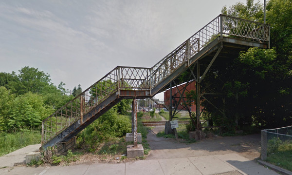 Pedestrian only bridge. No cycle infra, so a desire line across the tracks has been created. (Image Credit: Google Street View)