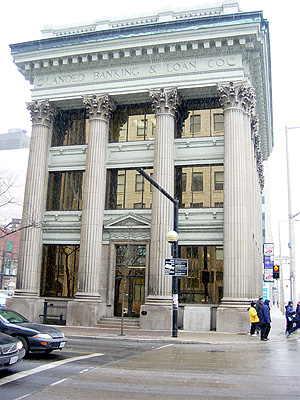 A beautiful old financial building sits mostly empty, its exterior adorned with surveillance camera warnings and For Rent signs.