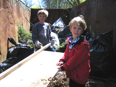 Young volunteers help drag a board into the dumpster.