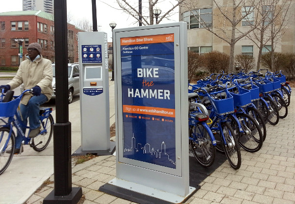 A cyclist rides a Hamilton Bike Share bike past the hub at Hunter GO Station