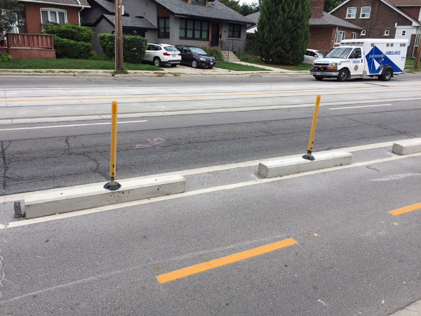 Bicycle lanes protected by concrete curb with knockdown sticks on top
